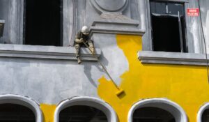 A Man Painting A Building With A Paintbrush