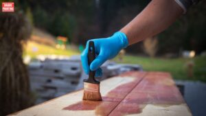 A Hand With Blue Gloves Painting A Wood Surface
