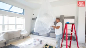 A Man Standing On A Ladder Holding A Plastic Bag Over A Ceiling