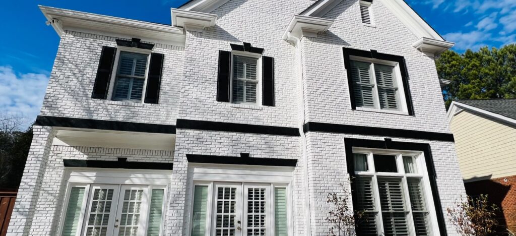 Painter standing on a ladder carefully painting the exterior trim of a house during daylight.
