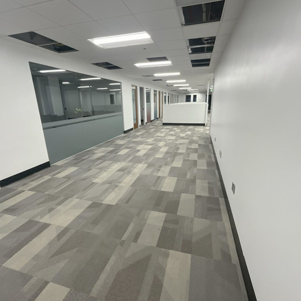 a hallway with a white wall and grey carpet
